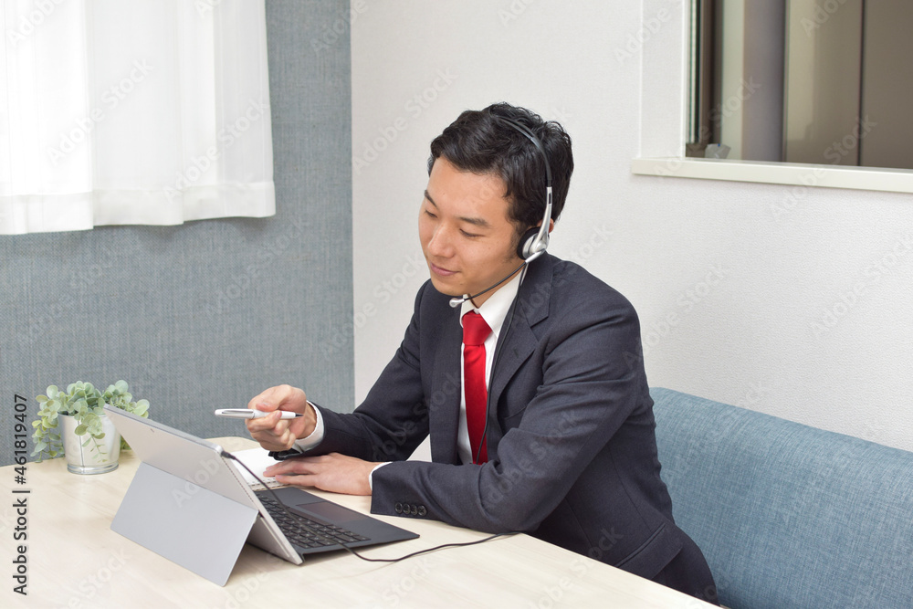 A young Asian man wearing a headset points a pen to his pc screen during telework A young Asian man wearing a headset points a pen to his pc screen during telework