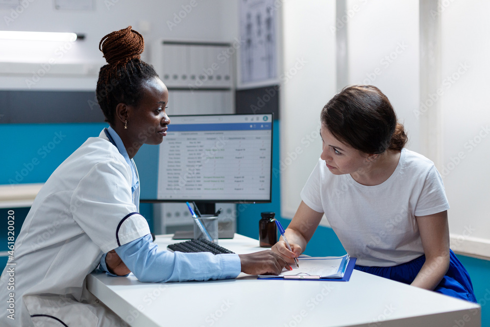 Obraz premium Sick patient signing medical documents discussing medication treatment with african american therapist in hospital office during clinical appointment. Doctor physician explaining disease symptoms