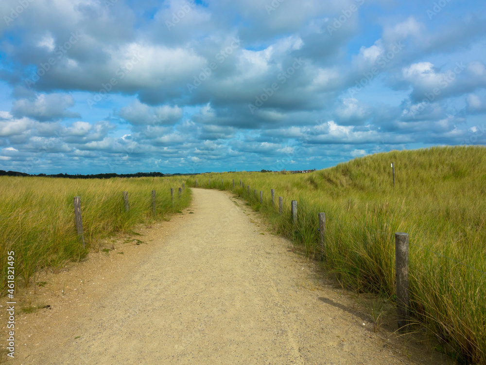 Summer landscape with view of sandy path with slopes or small hilly on the dunes against cloudy sky. Dutch north sea coastline, De Koog, Texel Island, Noord Holland, Netherlands.