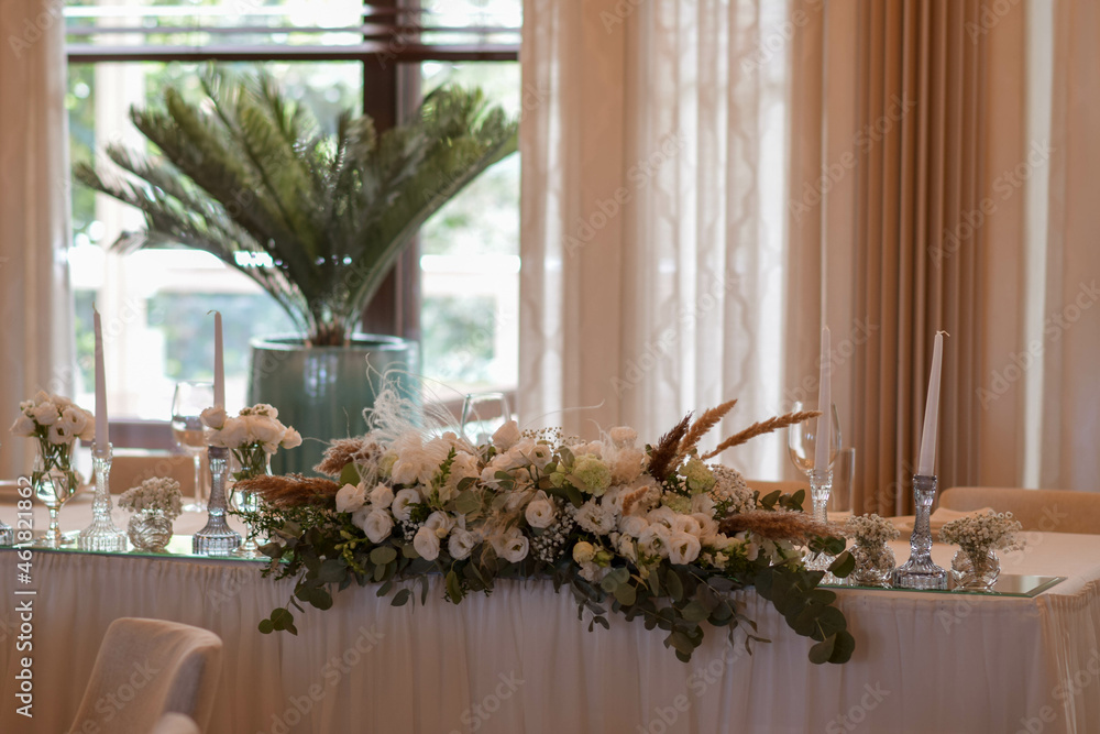White tablecloths with clear vases and white flowers and fern arrangements. Golden colored plates, peavh napkins, table numbers and mirror centerpieces.