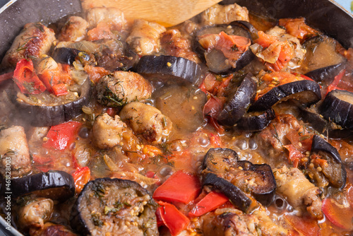 Stewed eggplants with sausage - cooking a delicious dish in a pan close-up