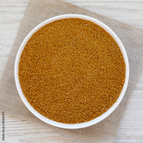 Organic Brown Sugar in a White Bowl on a white wooden surface, top view. Flat lay, overhead, from above.