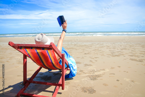 Asian tourist woman lounging on a deck chair by the sea holding a smartphone to take a selfie Enjoyed the sea excursions during the holidays. Concept of natural tourism in Thailand