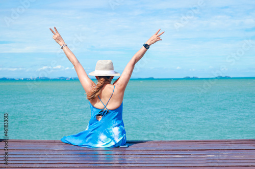 50 year old Asian woman sitting on a wooden floor by the sea She raised both hands, enjoying the sea during the holidays. Concept of natural tourism in Thailand