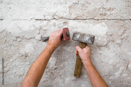 Young adult man hands using sledgehammer, metal stone chisel and removing old concrete on floor. Closeup. Point of view shot. Preparing for repair work of home. Flooring restoration. Top down view. photo