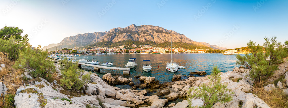 Panorama view of Makarska city, Croatia during the sunset. View with small boats and Biokovo mountains in the background. Summer weather, soft warm colors.