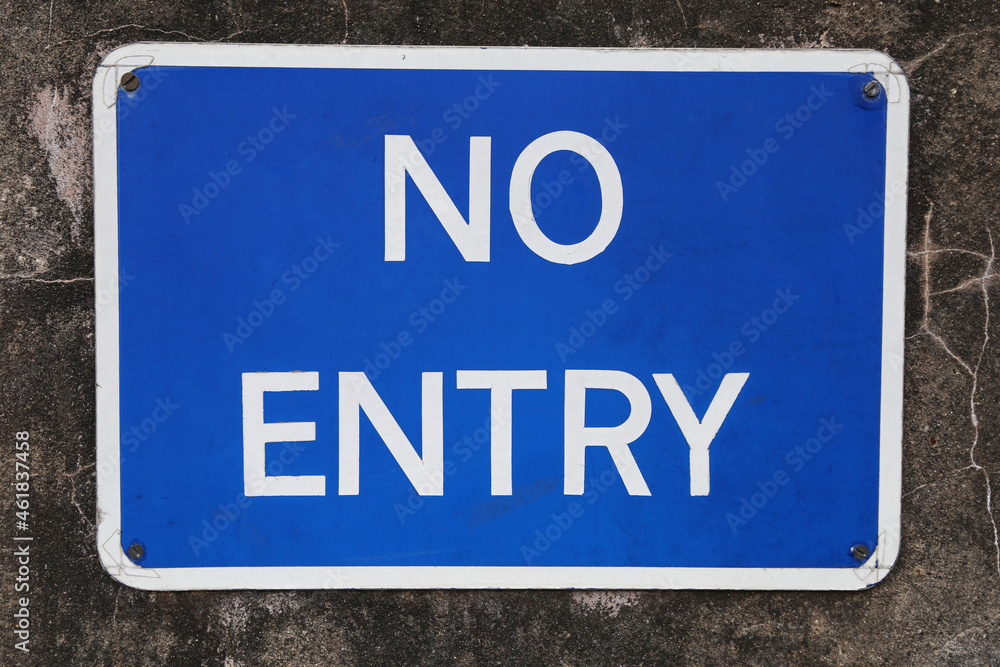 A blue and white no entry sign screwed to a concrete wall.