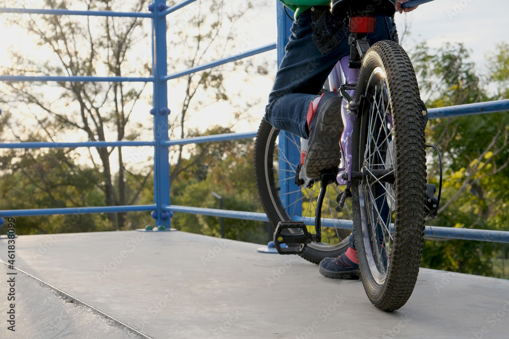 Obraz premium Child girl riding a bicycle in the park on a ramp slide.