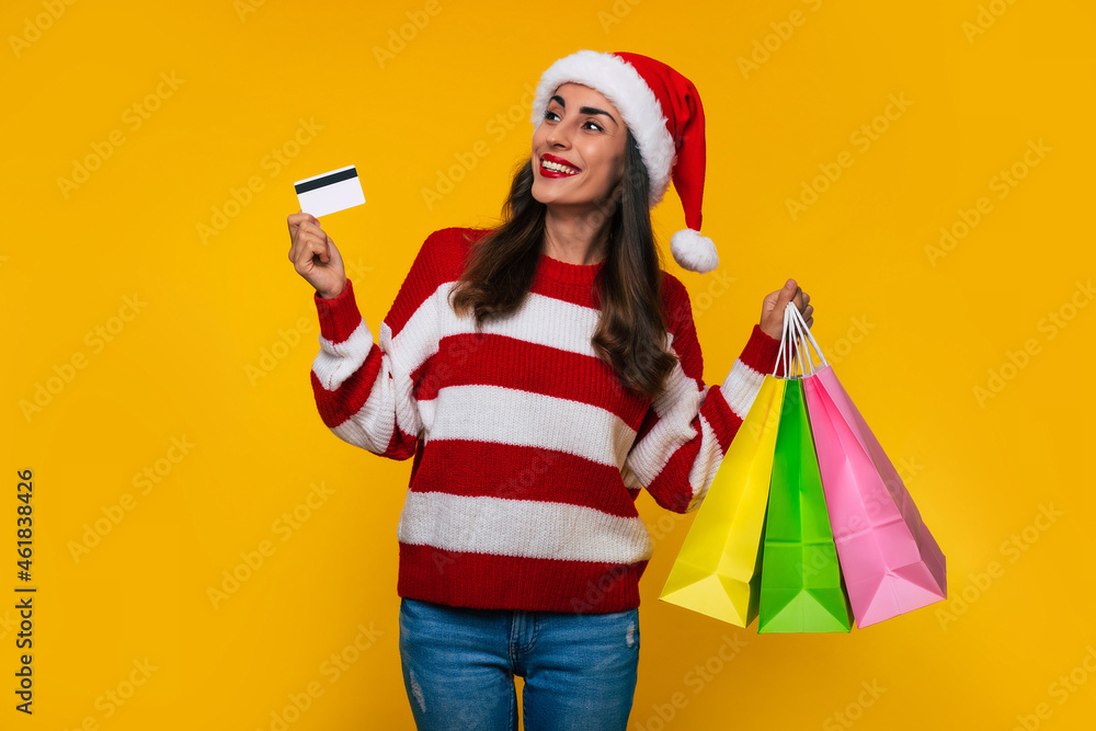 Happy stylish beautiful woman in Christmas hat with colorful shopping bags isolated on yellow background Happy stylish beautiful woman in Christmas hat with colorful shopping bags isolated on yellow background
