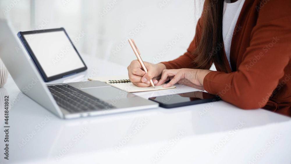 focus on hand young asian businesswoman holding pen writing note book while she using laptop and digital tablet working or meeting online focus on hand young asian businesswoman holding pen writing note book while she using laptop and digital tablet working or meeting online