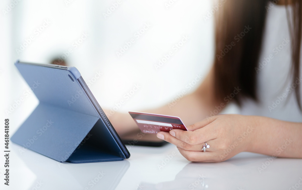 Focus on hand young asian woman holding mock up of creditcard and using digital tablet to shopping or paying online Focus on hand young asian woman holding mock up of creditcard and using digital tablet to shopping or paying online