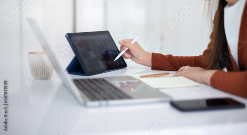 focus on hand young asian businesswoman using mobile app from digital tablet working and meeting online with laptop on white table