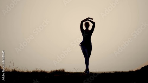the silhouette of a woman at sunset dancing gracefully ballet. elegant smooth swings of the hands