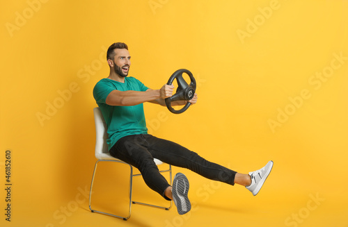 Tablou canvas Happy man on chair with steering wheel against yellow background