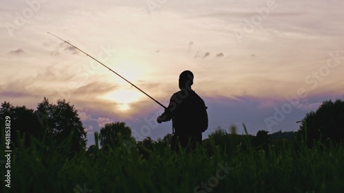 Silhouette of Adult Male Trying to Catch a Fish using Spinning Technique with Carbon Fiber Fishing Rod in Rays of Sun during Sunset 