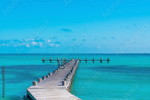 Flock of seagull birds flying over empty wooden jetty on blue tranquil sea water surface against sky