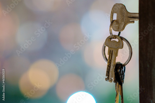 The keys with keyring in the door keyhole with blurred night lights background, selective focus © Luka