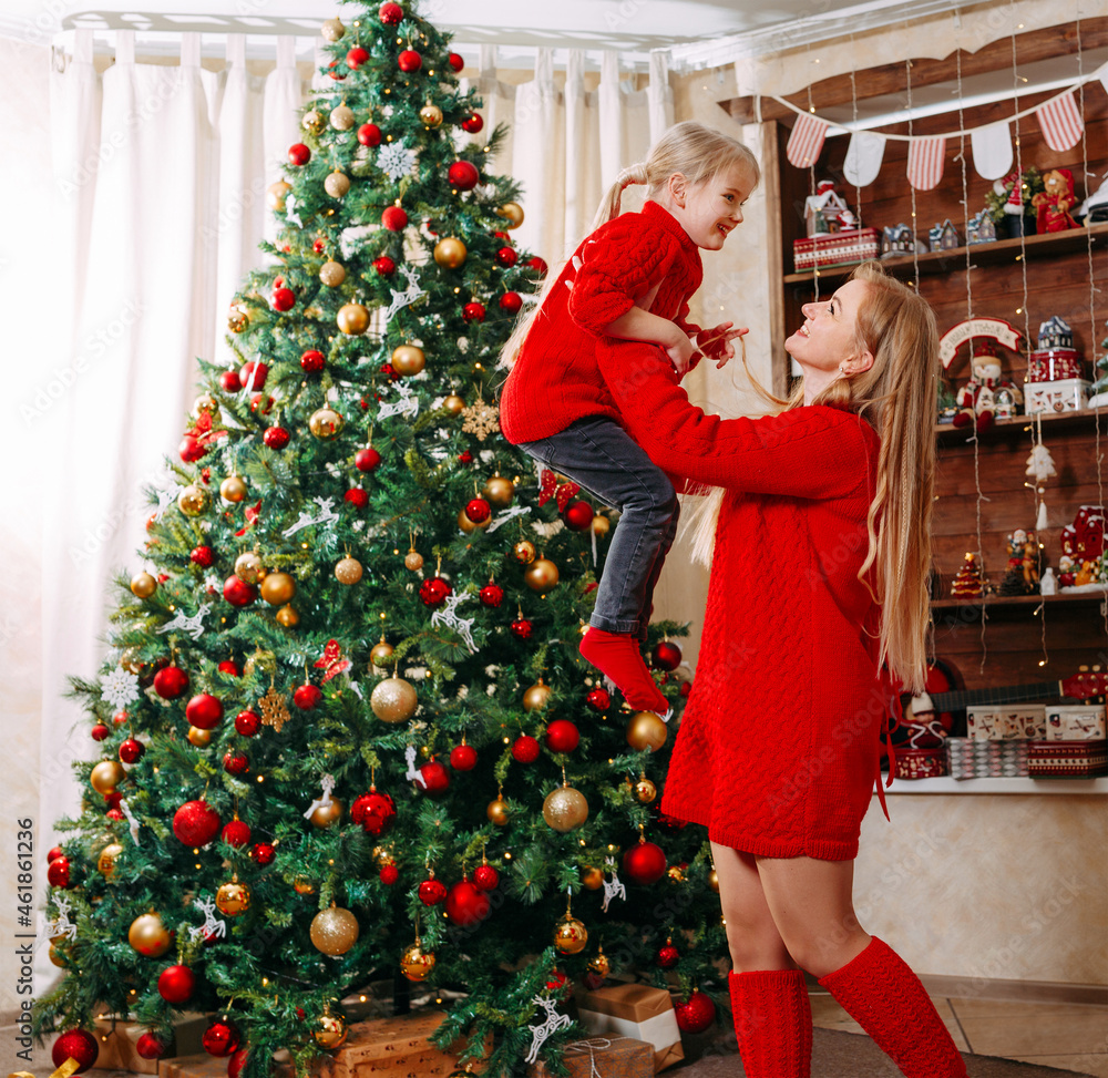 Mom and her daughter are having fun on Christmas Eve near a festively decorated Christmas tree.