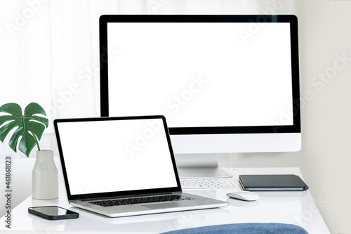 Mockup blank white screen laptop computer and desktop computer on white table.