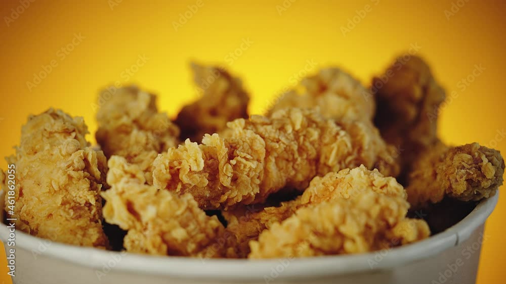 Big Bucket of crispy golden chicken wings, legs and strips. Side view over orange background Big Bucket of crispy golden chicken wings, legs and strips. Side view over orange background