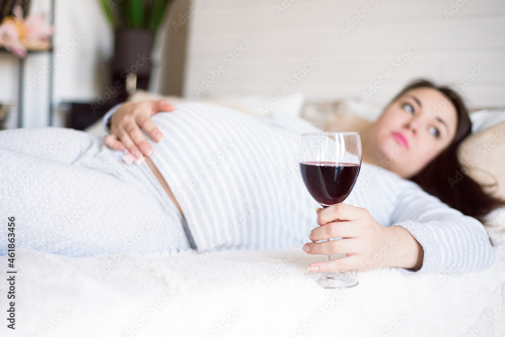 Pregnant woman keeping glass of wine. Future mother drinking alcohol while expecting little baby. Concept of unhealthy lifestyle and harmfulness.