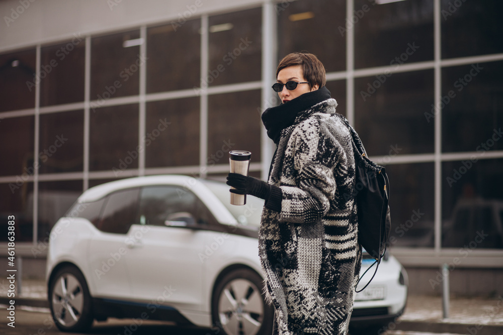 Fototapeta premium Woman drinking coffee and charging electro car