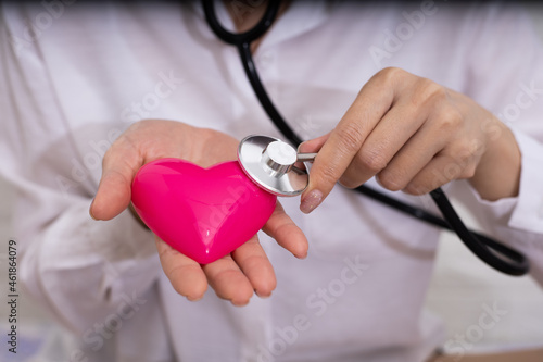 Feamle doctor with stethoscope examining red heart.