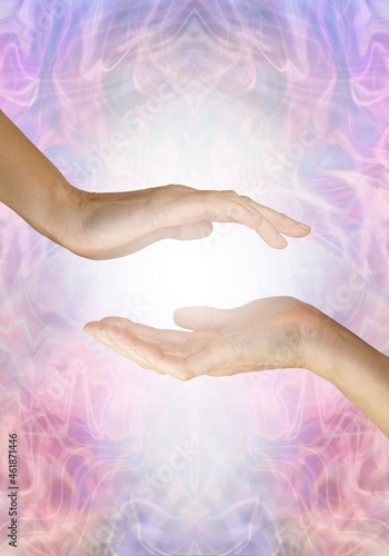 Sensing healing energy coming from palm chakra - female open hand hovering over another open hand with white light between against an ethereal blue  pink energy field background with space for text 
