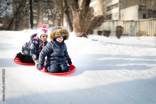 Little boy and girl moving from snowy hill on snow sled in winter