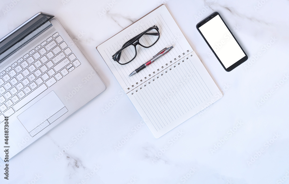 Flat lay of laptop, smartphone and eyeglasses with various stationeries on white marble tabletop Flat lay of laptop, smartphone and eyeglasses with various stationeries on white marble tabletop