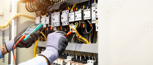 Electrical engineer using digital multi-meter measuring equipment to checking electric current voltage at circuit breaker and cable wiring system in main power distribution board. photo