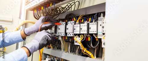 Electrical engineer using digital multi-meter measuring equipment to checking electric current voltage at circuit breaker and cable wiring system in main power distribution board. photo