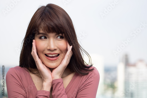 Excited and surprised asian woman smiles and looks up in urban outdoor environment