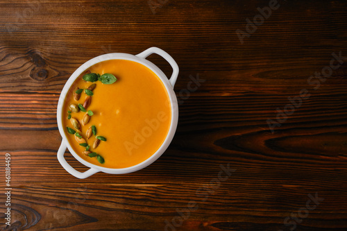 Pumpkin creamy soup in a bowl with seeds and basil