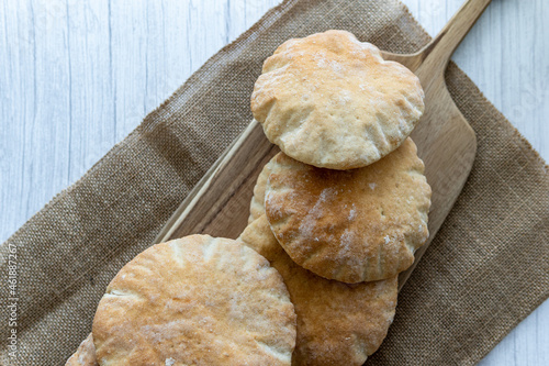 Pita bread on a wooden board, hot from the oven. Homemade, freshly baked gluten-free flatbread or pitta. Fluffy, round bread that can be stuffed with food. Rustic cloth and white wooden background.