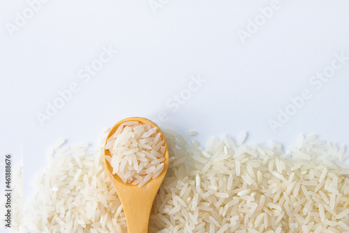 Uncooked dry rice in wooden spoon on white background.