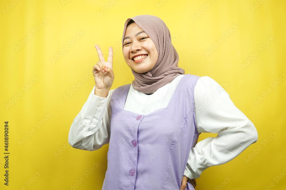 Beautiful young asian muslim woman pouting with v-signed hands, ok, good job, agreement, victory, looking at camera isolated on yellow background Beautiful young asian muslim woman pouting with v-signed hands, ok, good job, agreement, victory, looking at camera isolated on yellow background