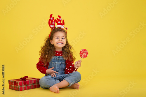 Portrait of happy little girl Christmas holding present box and looking at camera on yellow background 