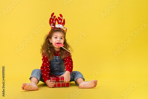 Portrait of happy little girl Christmas holding present box and looking at camera on yellow background 