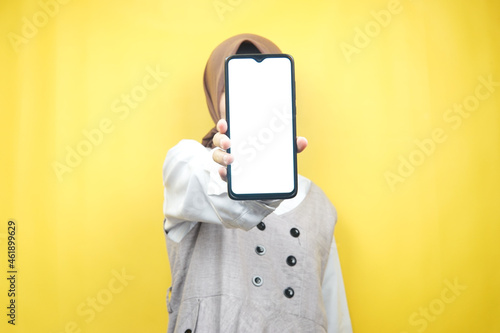 Muslim woman with hands holding smartphone, promoting app, promoting something, isolated on yellow background, advertising concept