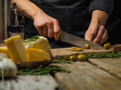 A professional chef is cutting olives on a cutting board. Ingredients. wood texture. Close-up. Cooking salad, pizza, focaccia. Restaurant, hotel, cafe. cookbook. Color image.