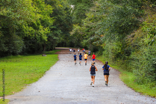 teenagers running down a dirt footpath on a hiking trail covered with gorgeous autumn leaves surrounded by lush green and autumn colored trees at Cochran Shoals Trail in Marietta USA photo