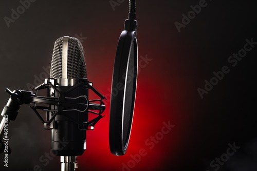 Professional microphone and pop filter on a black-red background. Broadcasting, television, singing, music, purity of sound. Minimalism. Close-up.