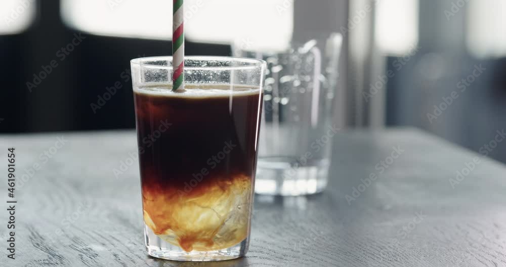 Slow motion add straw to espresso tonic ice ball in tumbler glass on black wood table closeup Slow motion add straw to espresso tonic ice ball in tumbler glass on black wood table closeup