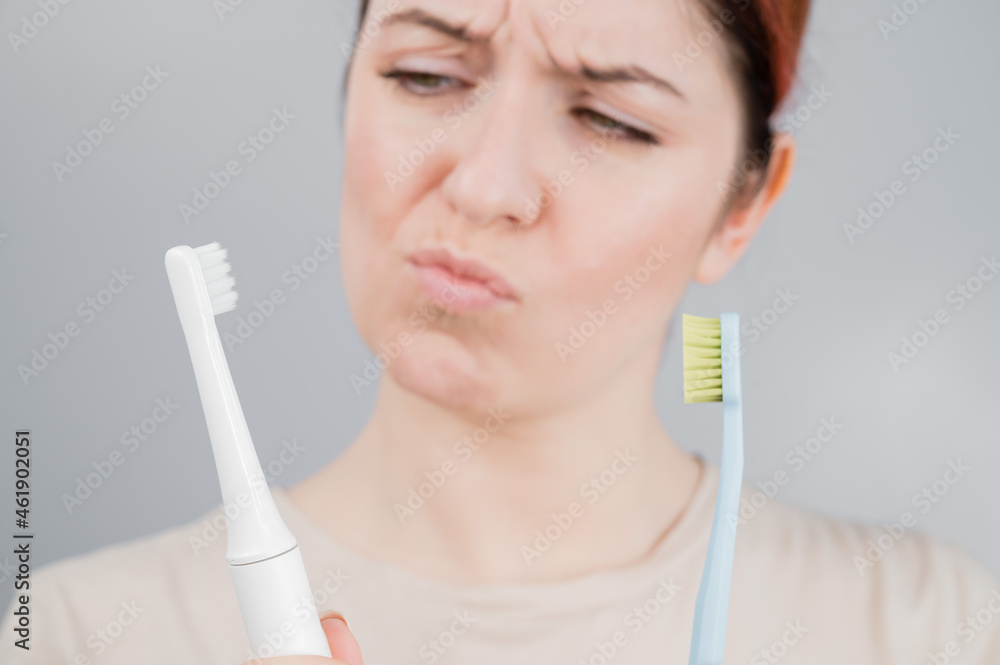 Happy woman compares a toothbrush with an electric one. The girl chooses oral hygiene products Happy woman compares a toothbrush with an electric one. The girl chooses oral hygiene products
