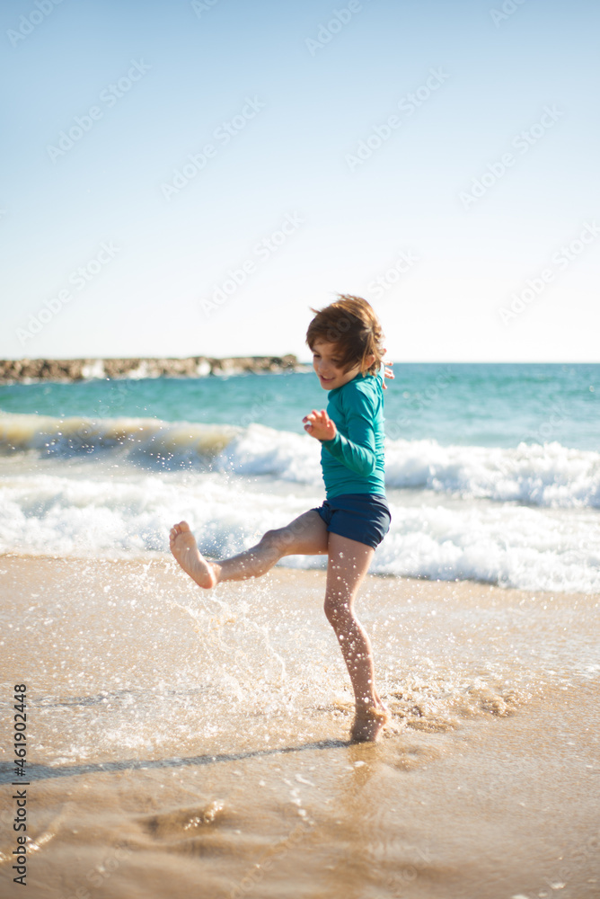 Little boy splashing water at beach. Child playing in waves at sea cost, smiling, moving. Family, vacation, outdoor activity concept