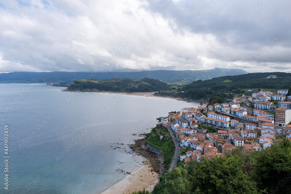 view of the fishing village of Lastres from the viewpoint of San Roque, with the mountains of Asturias in the background and La Griega and Lastres beaches, cloudy sky, horizontal