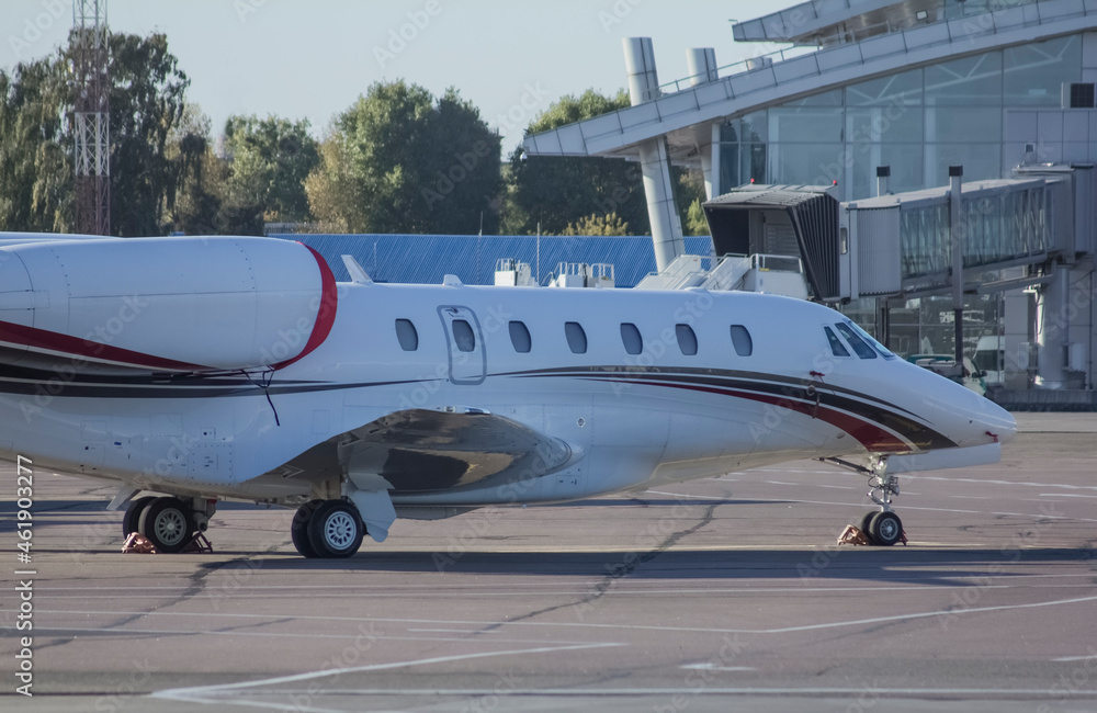 A twin-engine jet business plane with landing lights on is driving along the airport taxiway against the background of a clear sky 