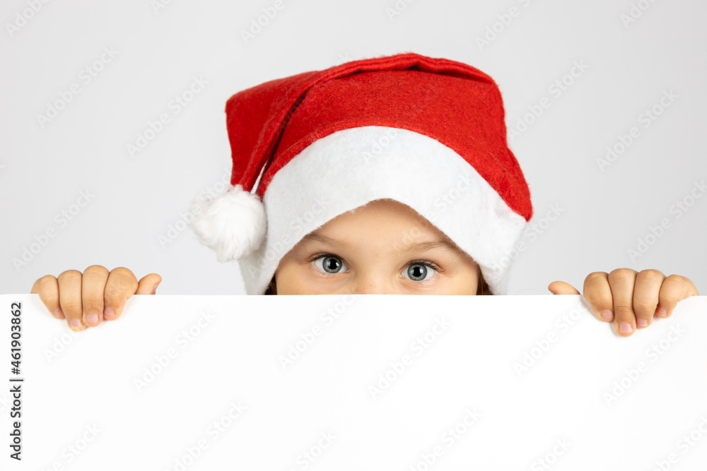 portrait of cute child in red Santa Claus hat hiding face behind white blank banner isolated on white background with copy space. portrait of cute child in red Santa Claus hat hiding face behind white blank banner isolated on white background with copy space.