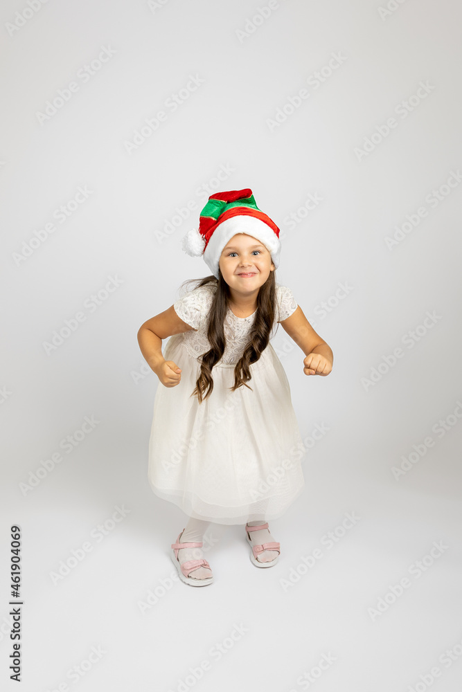full-length portrait of cheerful girl in white dress and Christmas gnome hat dancing and enjoying holidays, isolated on white background.